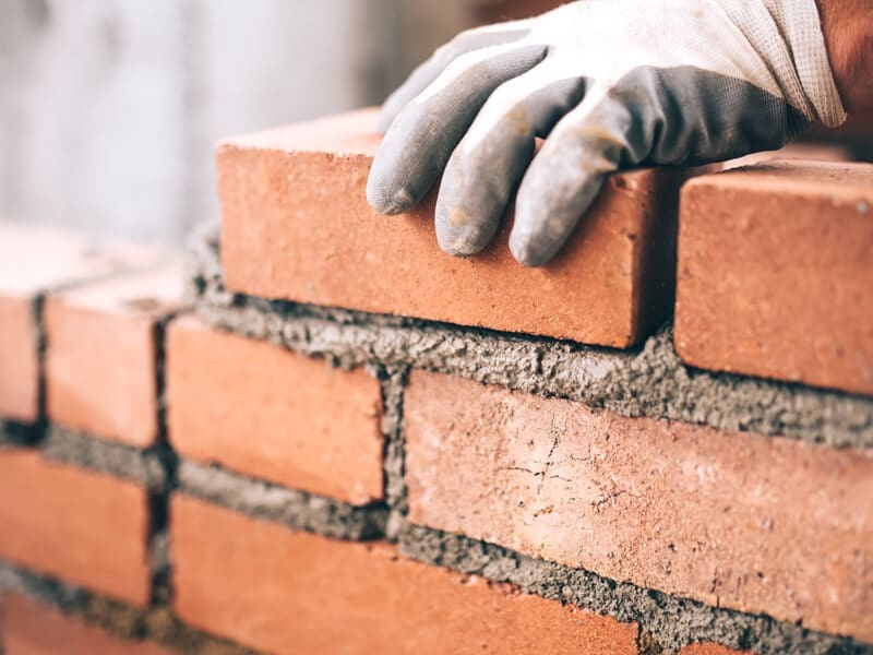 Stone Haven Developments A gloved hand places a brick onto a wall under construction, with wet mortar visible between the bricks—a testament to Stone Haven Developments’ commitment to quality craftsmanship. Ontario
