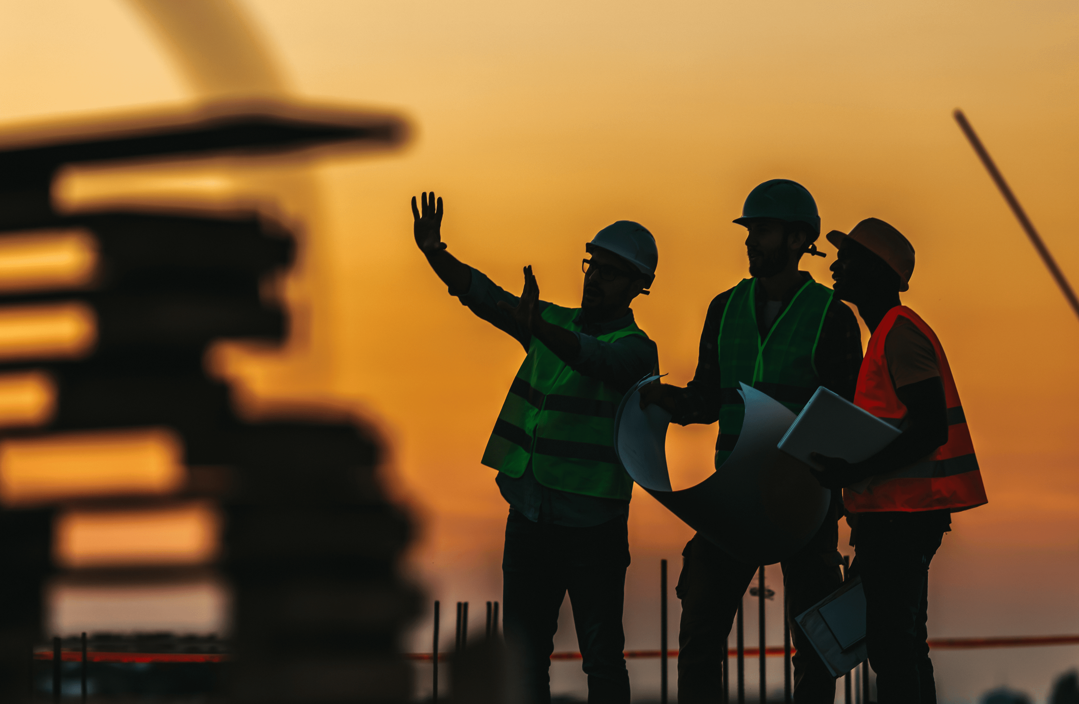 Stone Haven Developments Three construction workers wearing safety gear discuss plans at a building site during sunset, with one gesturing and holding documents—another step forward for Stone Haven Developments. Ontario