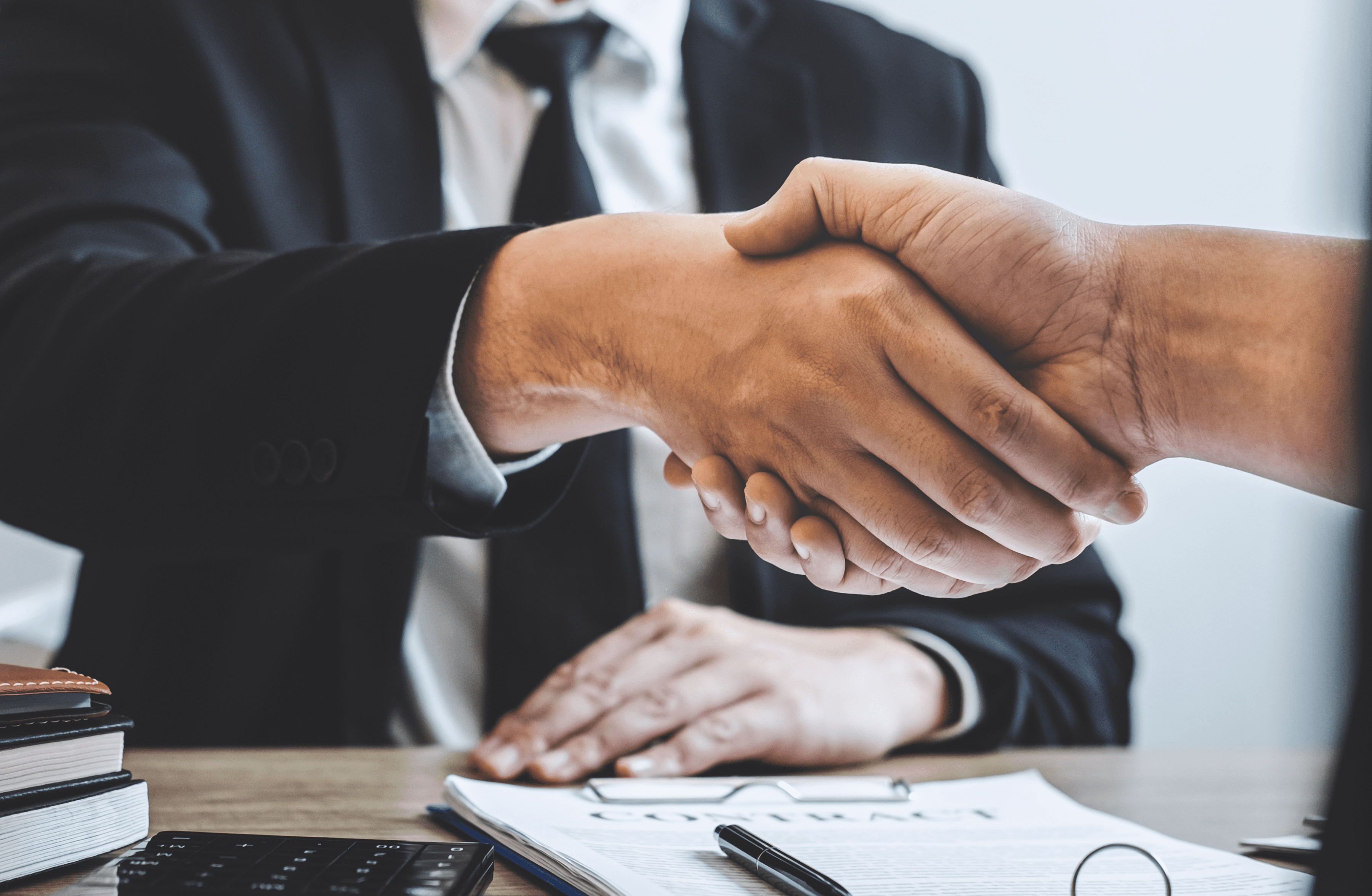 Stone Haven Developments Two people in business attire shake hands over a desk with documents, including a visible contract and calculator, marking the start of a new partnership with Stone Haven Developments. Ontario
