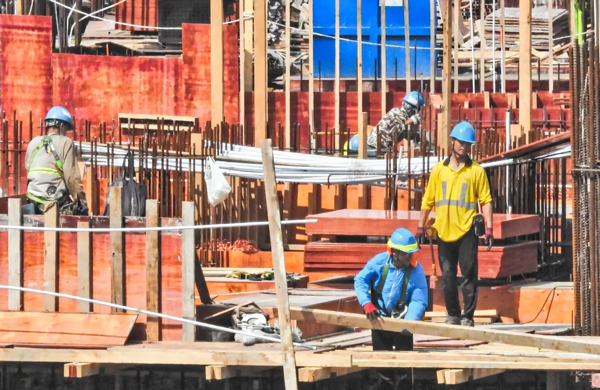 Stone Haven Developments Four construction workers wearing helmets and safety gear work on a building site with exposed steel rebar and wooden planks in daylight. Ontario