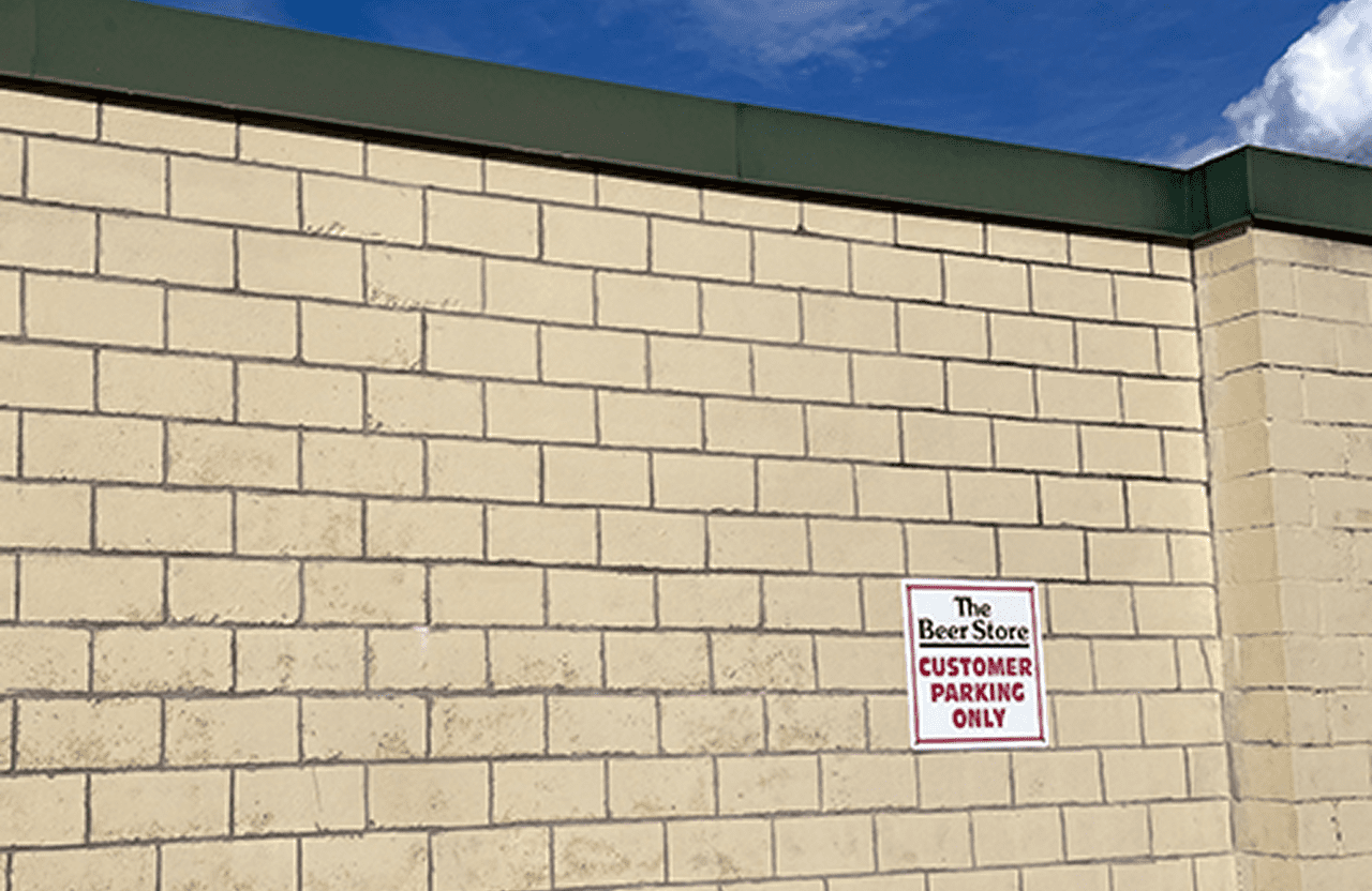 Stone Haven Developments A tan brick wall with a green trim features a sign that reads, "The Beer Store Customer Parking Only" under a partly cloudy sky. Ontario