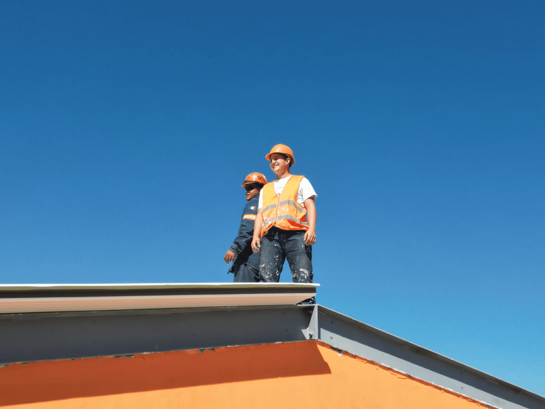 Stone Haven Developments Two construction workers in safety helmets and vests stand on the edge of a building roof under a clear blue sky. Ontario