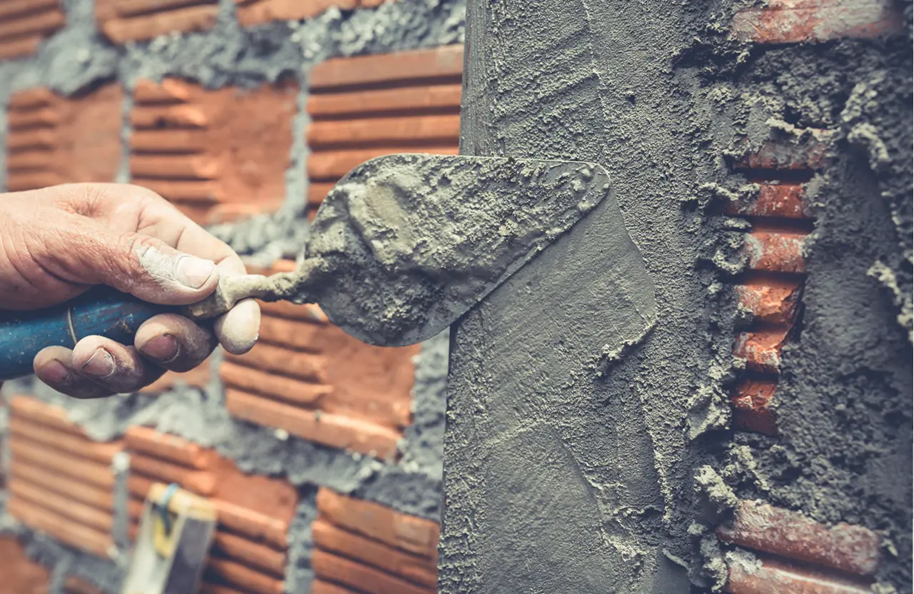 Stone Haven Developments A hand uses a trowel to spread wet cement on a brick wall during construction. Ontario