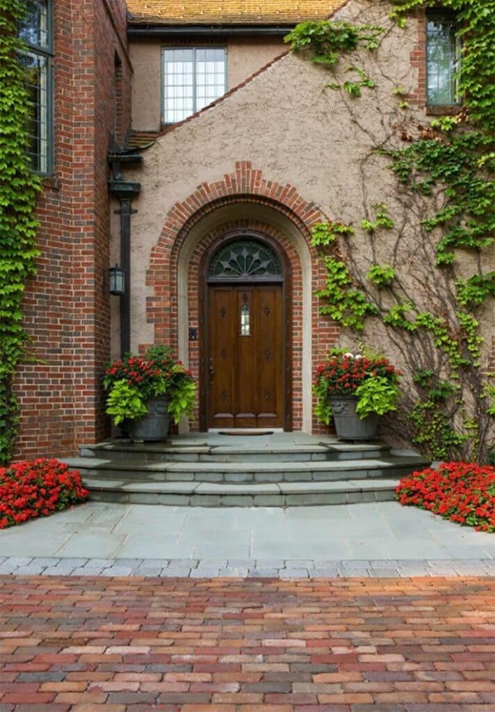 Stone Haven Developments A wooden arched front door with a fanlight window, surrounded by ivy-covered brick and stucco walls, potted plants, and red flowers on stone steps. Ontario