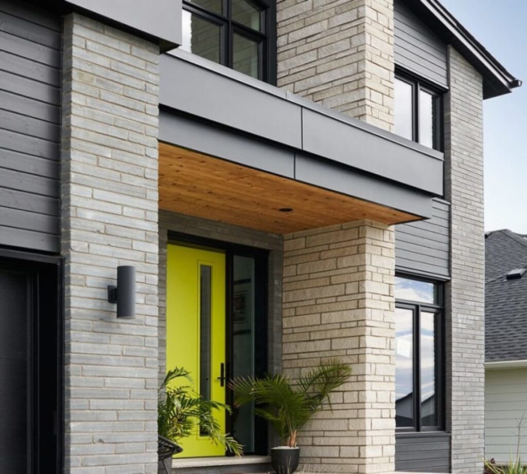 Stone Haven Developments Modern house exterior with light brick and dark siding, featuring a bright yellow front door, potted plants, and large windows. Ontario