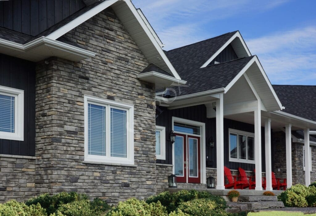 Stone Haven Developments A modern house with stone and dark siding, white trim, and a covered front porch featuring red chairs. Shrubs line the walkway in front. Ontario