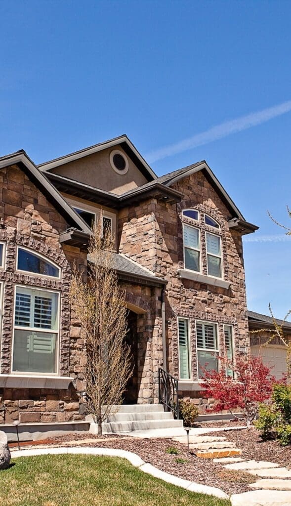 Stone Haven Developments Two-story house with stone exterior, multiple windows with white shutters, front steps, and landscaped yard with small trees and shrubs. Ontario