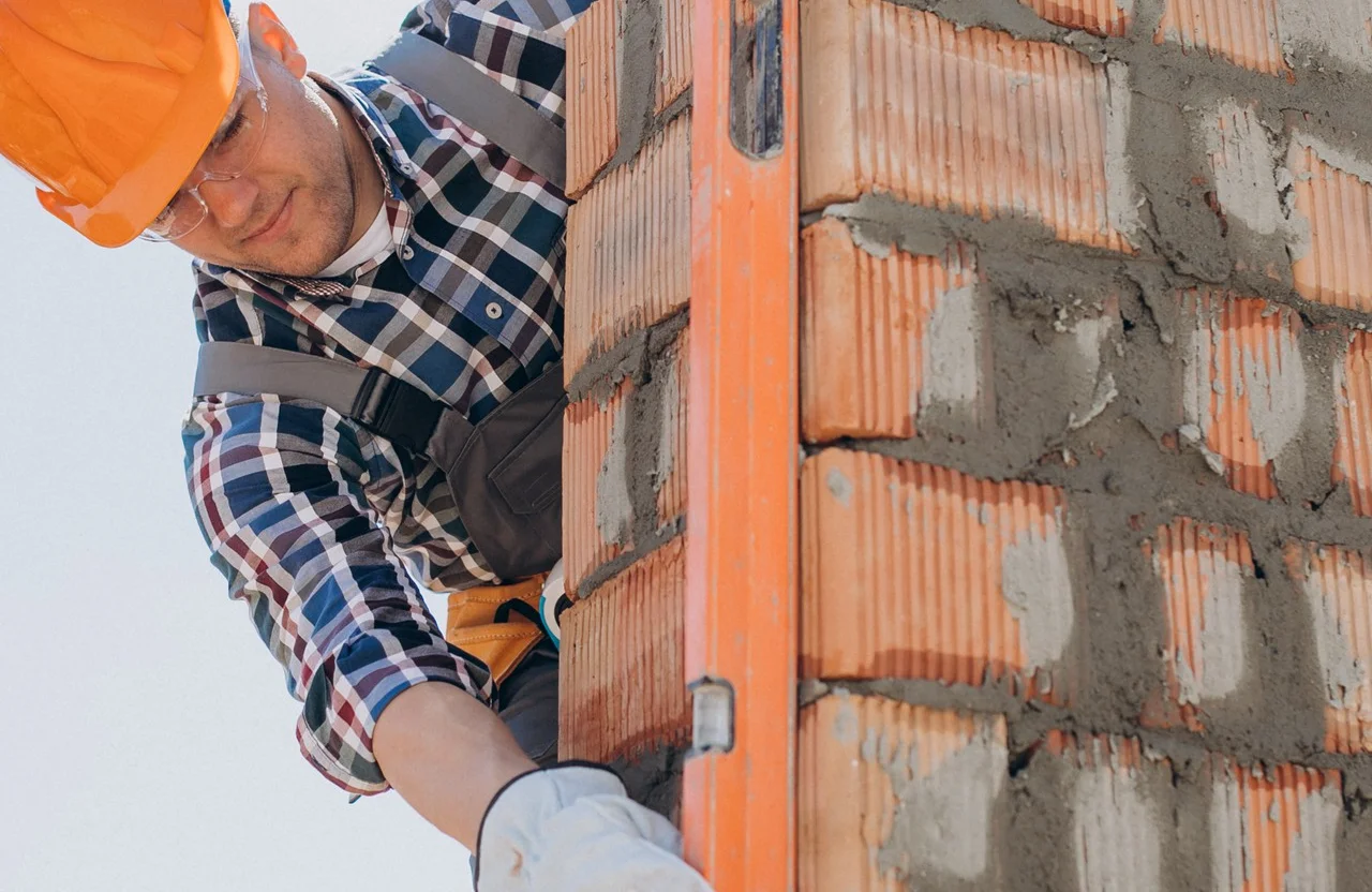 Stone Haven Developments Construction worker in a hard hat checks the alignment of a brick wall using an orange spirit level. Ontario