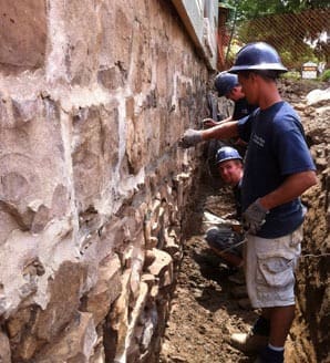 Stone Haven Developments Three construction workers in safety helmets repair or inspect a stone foundation wall at an outdoor work site. Ontario
