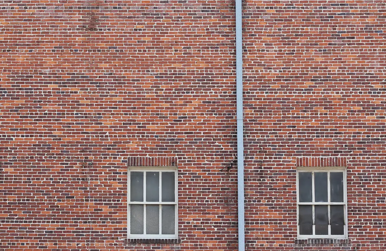 Stone Haven Developments A brick wall with two rectangular windows and a vertical metal pipe running between them. Ontario