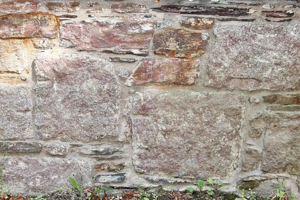 Stone Haven Developments A close-up view of an old stone wall with irregularly shaped rocks and visible mortar, with some grass and plants at the base. Ontario