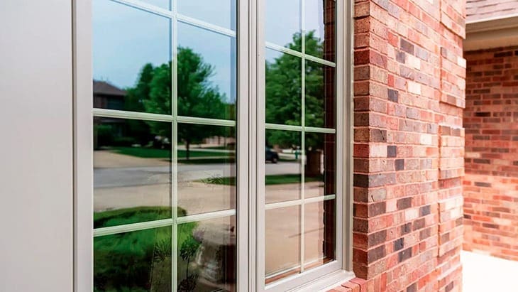 Stone Haven Developments A close-up of a brick house exterior shows a large window with white grid-style panes, reflecting trees, houses, and a street in the background. Ontario
