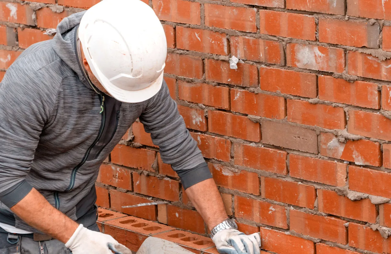 Stone Haven Developments Person wearing a white hard hat and gloves builds a brick wall, using a trowel to apply mortar between bricks. Ontario