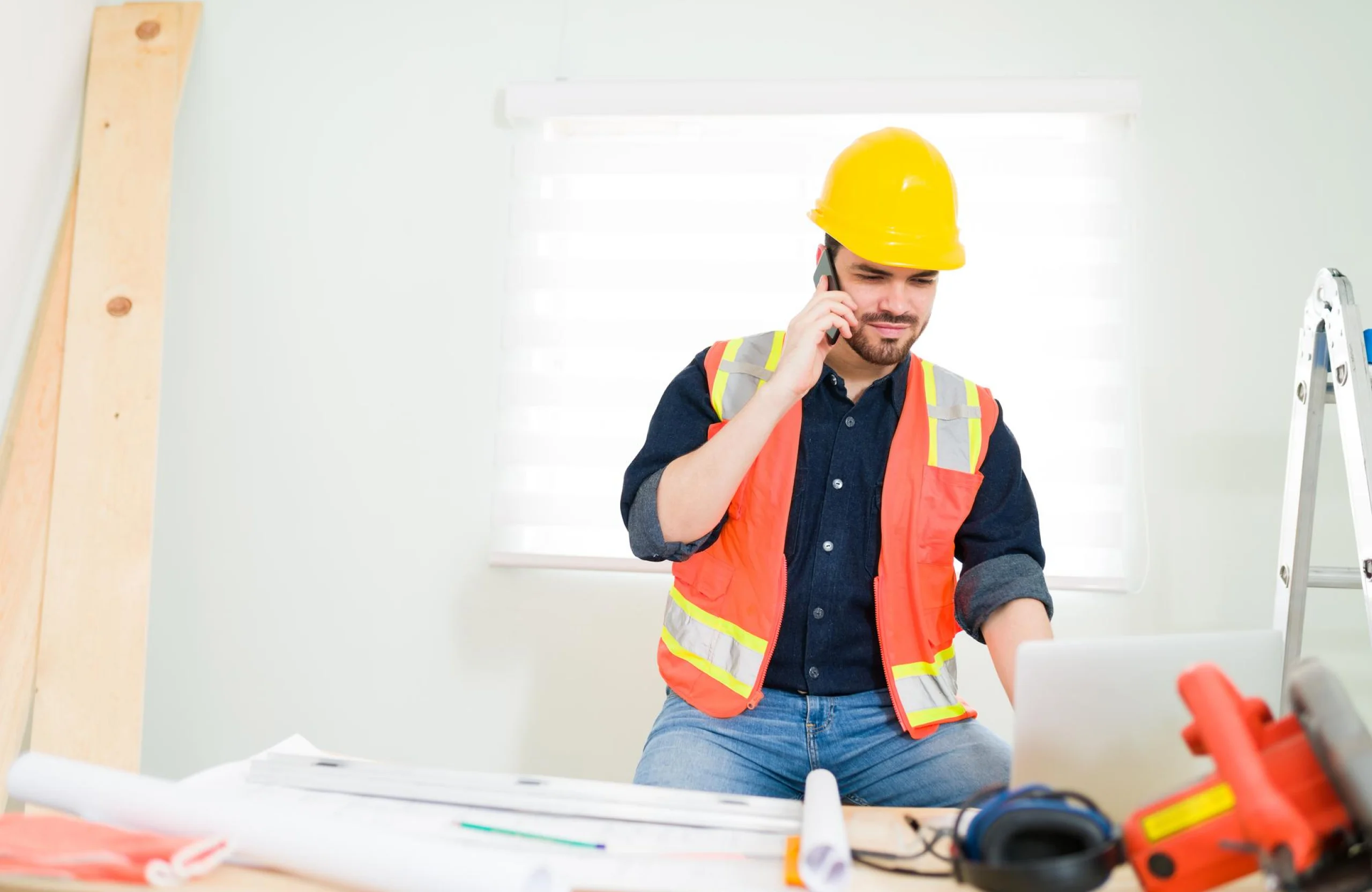 Stone Haven Developments A construction worker in a safety vest and helmet talks on a phone while using a laptop at a desk with blueprints and tools. Ontario