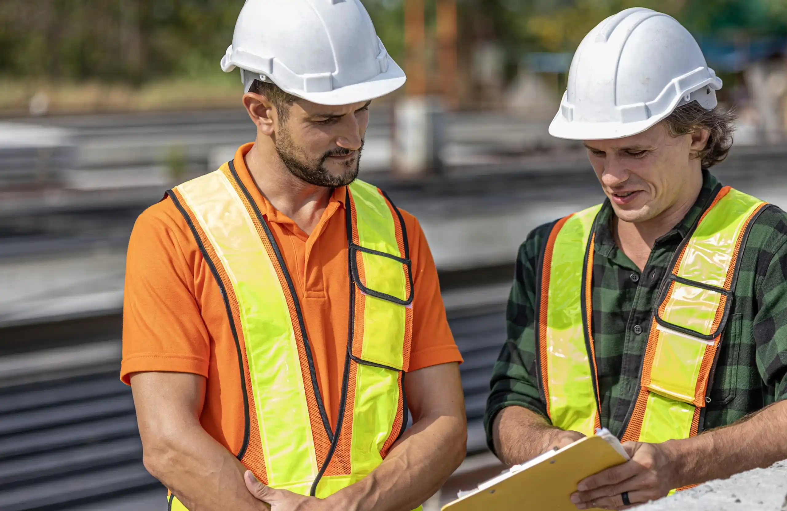 Stone Haven Developments Two construction workers wearing reflective vests and white hard hats review documents on a clipboard at an outdoor work site. Ontario