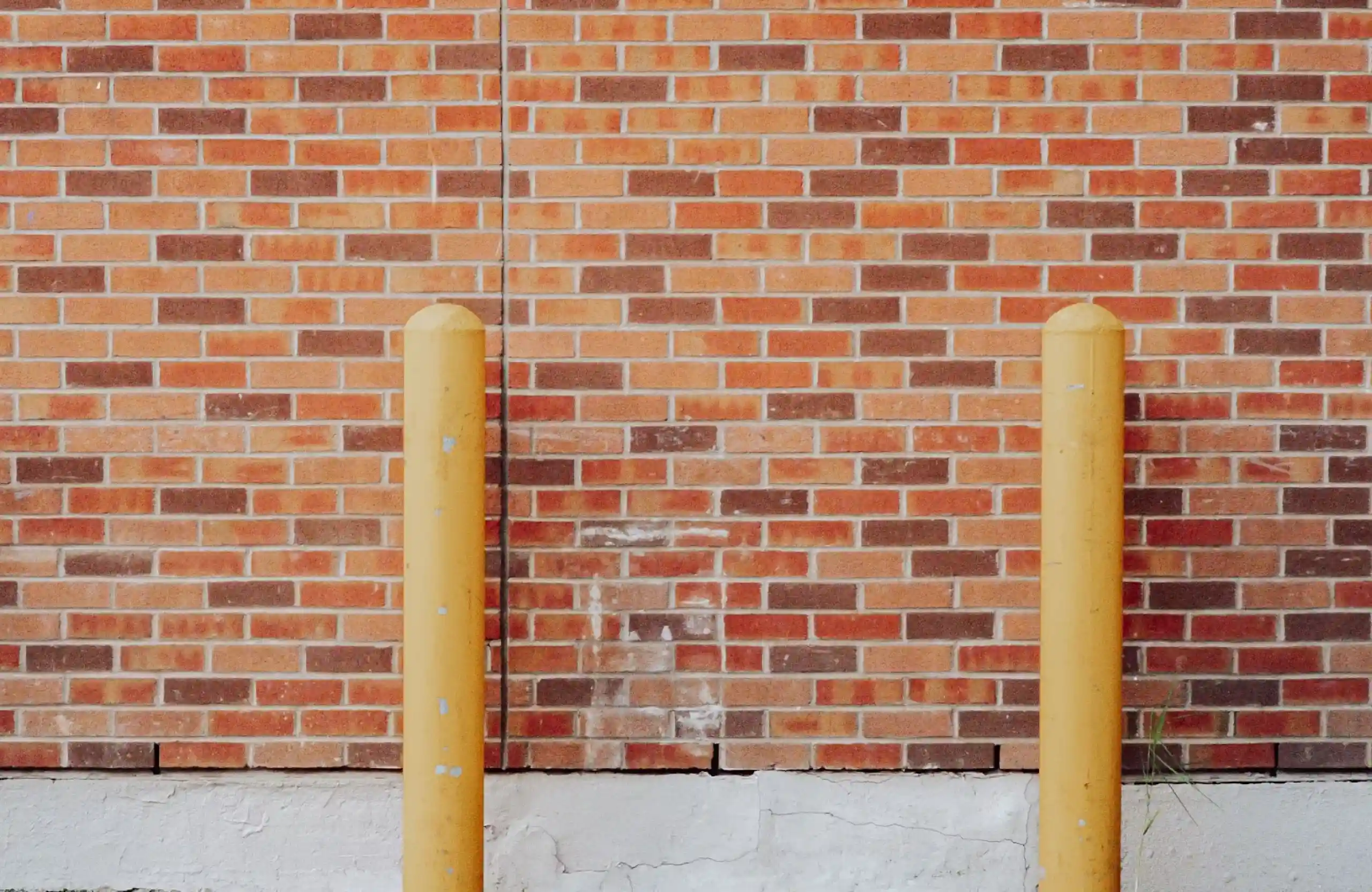 Stone Haven Developments Two yellow bollards stand in front of a red brick wall with a cracked white concrete base. Ontario