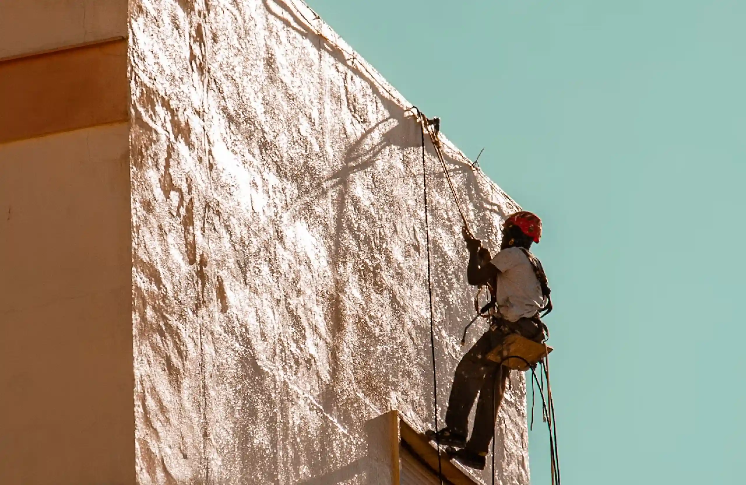 Stone Haven Developments A worker wearing safety gear is suspended on ropes while painting the exterior wall of a building under bright daylight. Ontario
