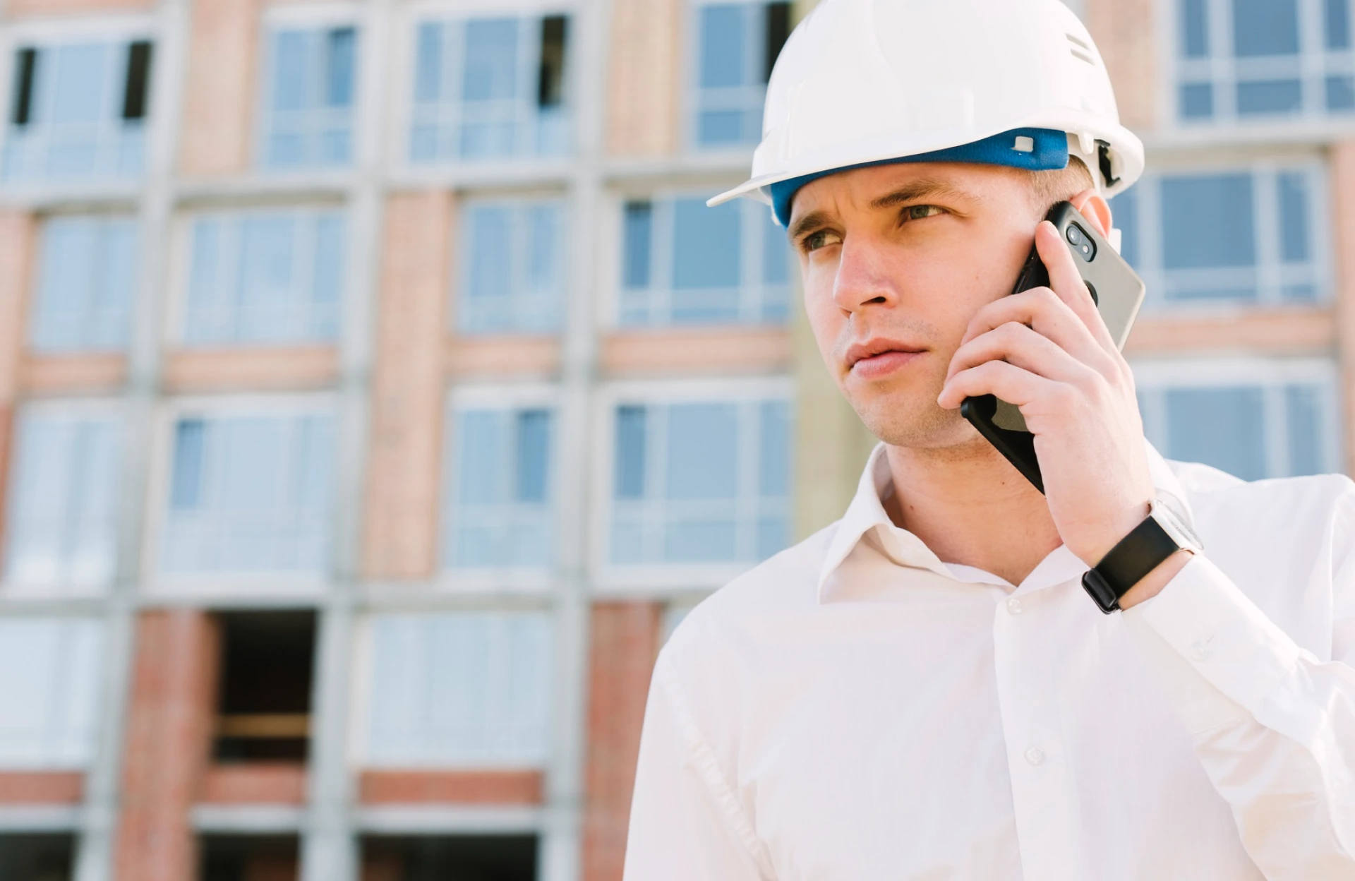 Stone Haven Developments A man wearing a white hard hat and dress shirt is talking on a smartphone at a construction site with a building in the background. Ontario
