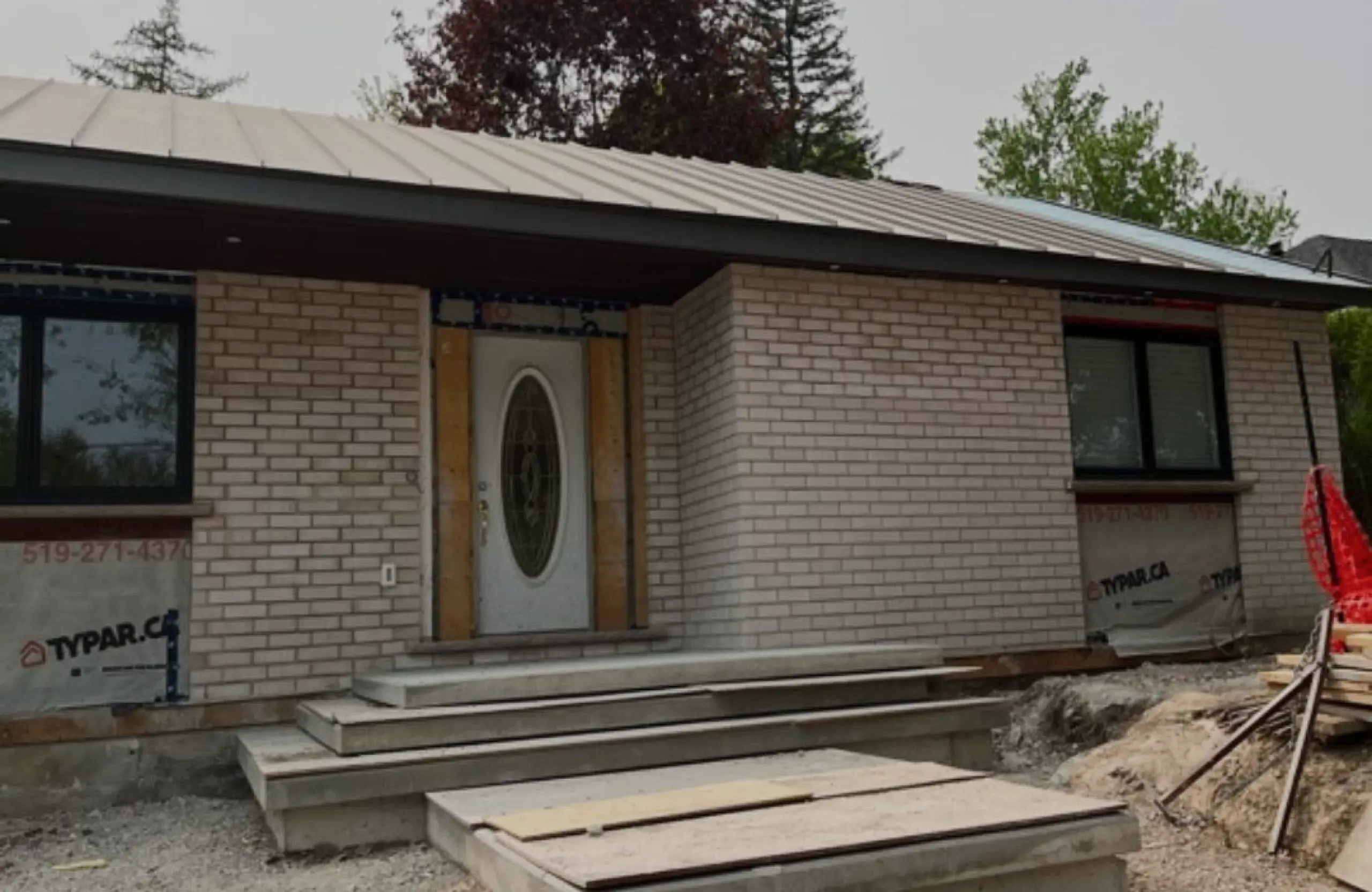 Brick home renovation in progress with new front door, steps, and Typar house wrap in Ontario