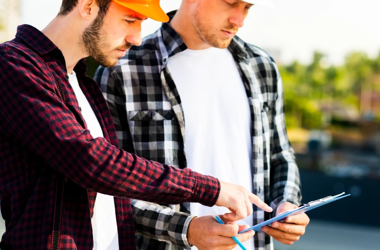 Two contractors in hard hats reviewing a clipboard together on a construction site in Ontario