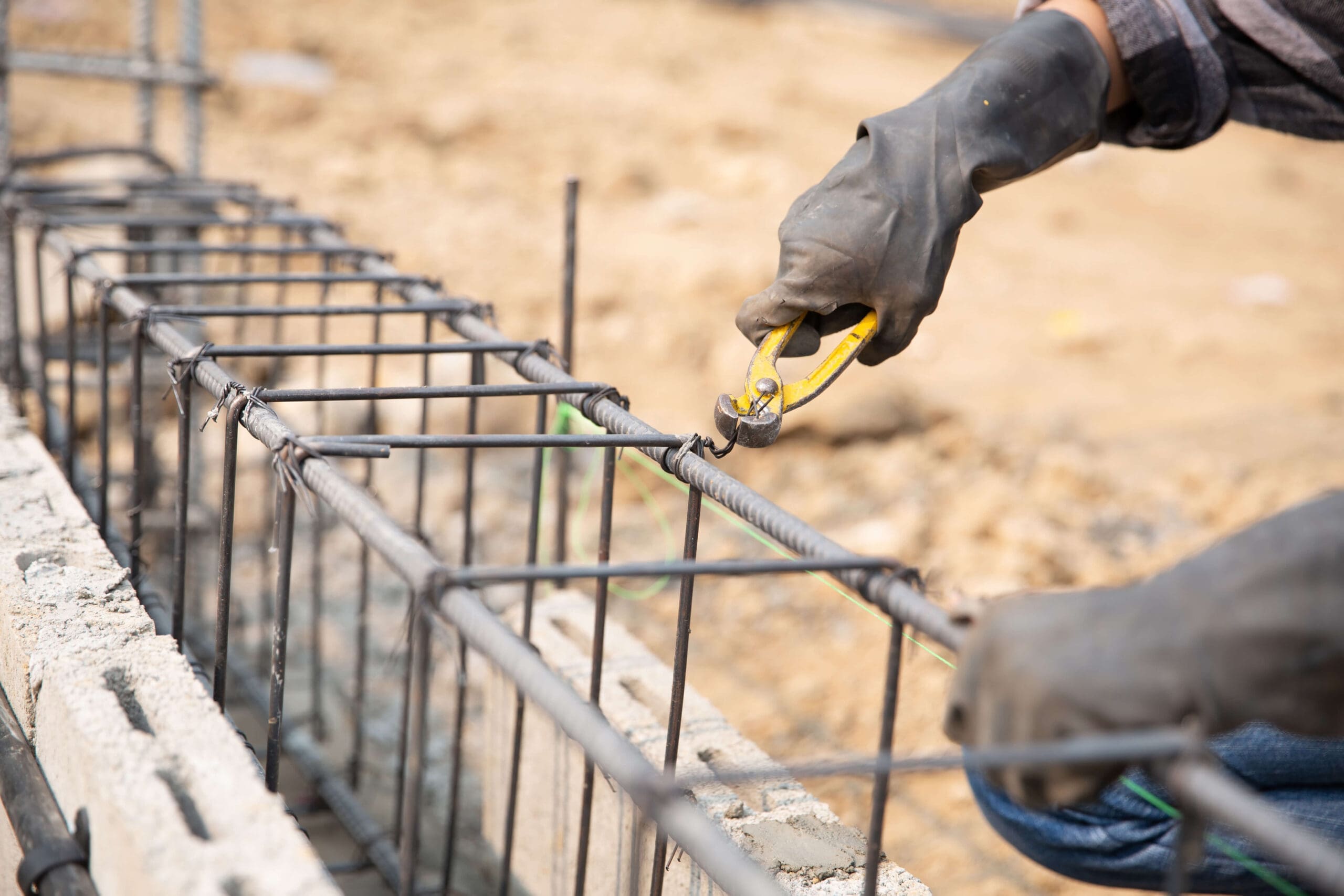 Stone Haven Developments A person wearing gloves uses pliers to cut wire tied around steel reinforcement bars at a Stone Haven Developments construction site. Ontario