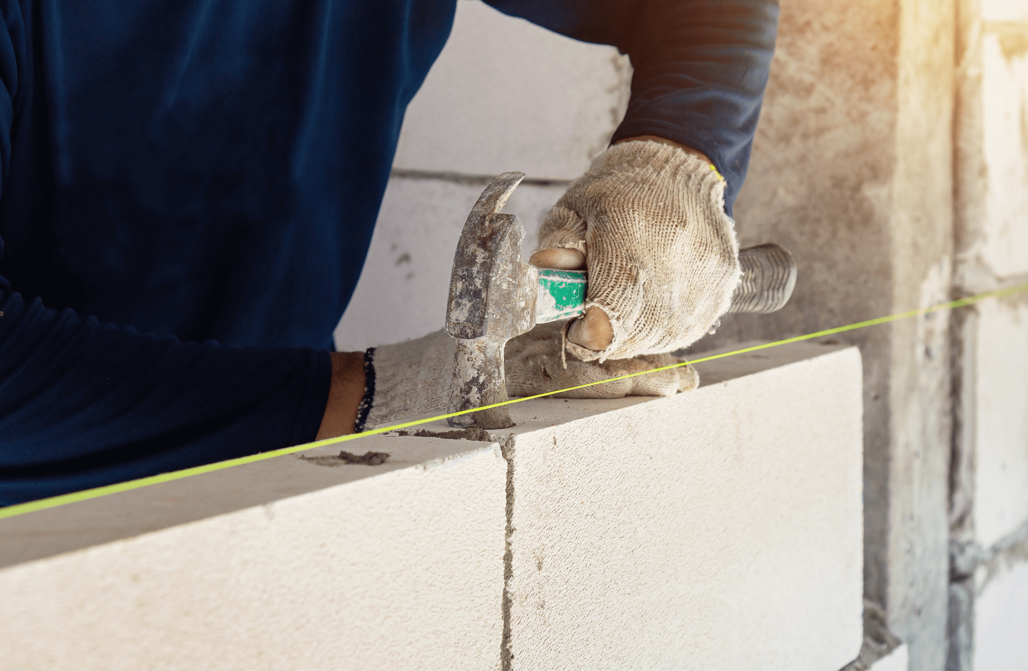 Stone Haven Developments A person wearing gloves uses a hammer and a measuring tool to align a cinder block wall with a yellow guide string at a Stone Haven Developments construction site. Ontario
