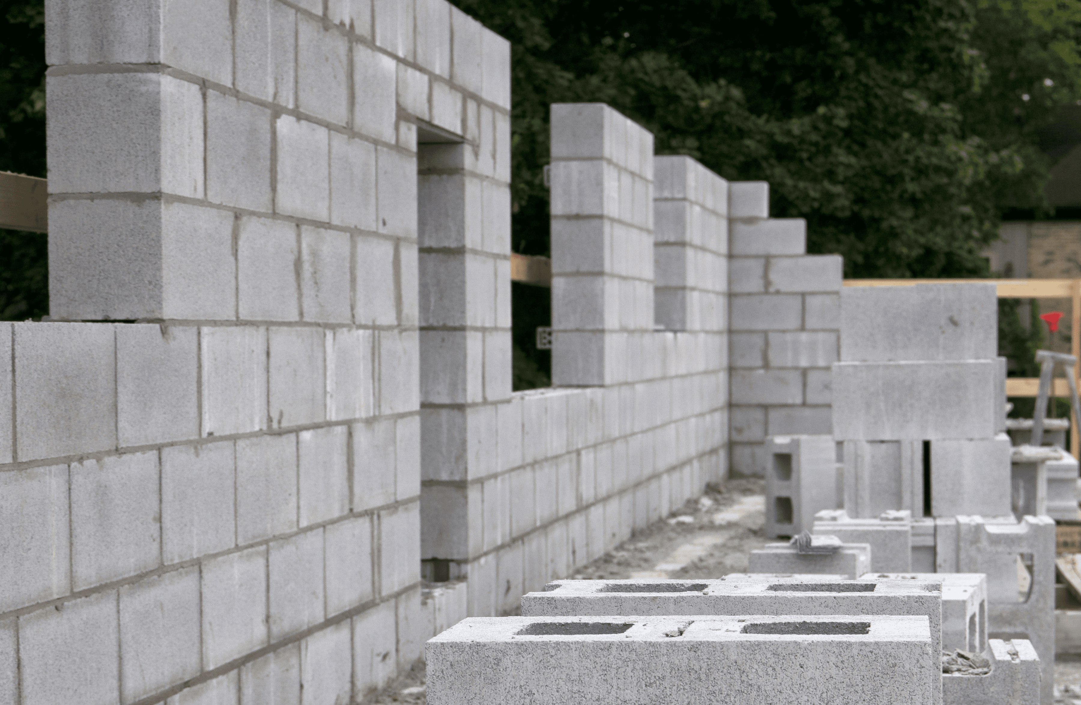 Stone Haven Developments Partially constructed concrete block wall with window openings by Stone Haven Developments, stacks of unused cinder blocks in the foreground, and trees in the background. Ontario