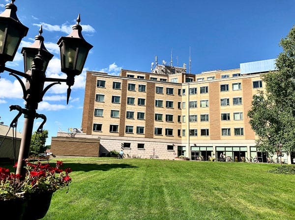 Stone Haven Developments A five-story brick building by Stone Haven Developments features many windows, a well-kept lawn, and a vintage street lamp in the foreground under a clear blue sky. Ontario